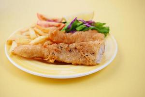 Fish fillet, lemon , chips and potato mash on yellow background photo