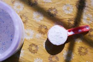 Washing powder in plastic spoon on table top view photo