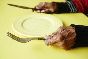 senior women holding cutlery with empty plate on yellow background photo