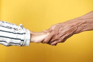 close up of child hand holding senior women's hand against yellow background photo