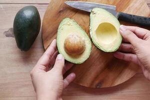 women hand cutting slice of avocado with knife, photo
