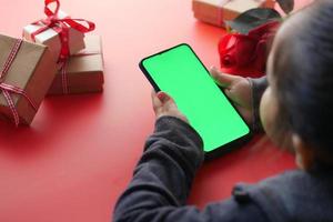 vista superior de la mano del niño sostenga el teléfono inteligente y la caja de regalo sobre fondo rojo foto