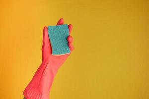 hand in rubber gloves holding sponge against yellow