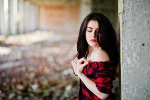 Portrait girl with red lips wearing a red checkered shirt with bare shoulders posed sexy background abadoned place. photo