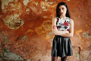 Young goth girl on black leather skirt posed against grunge wall. photo