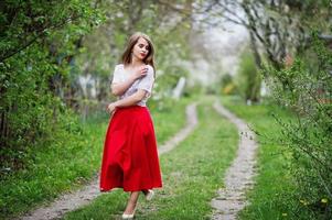 Portrait of beautiful girl with red lips at spring blossom garden, wear on red dress and white blouse. photo