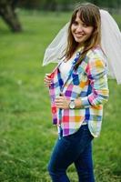 Portrait of brunette girl on checkered shirt, jeans and veil at hen party.