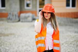 mujer ingeniera constructora con chaleco uniforme y casco protector naranja contra el nuevo edificio. tema de bloque de vivienda de propiedad. foto