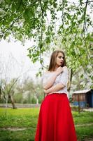 Portrait of beautiful girl with red lips at spring blossom garden, wear on red dress and white blouse. photo