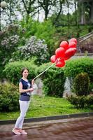 Portrait of a gorgeous beautiful bridesmaid in casual clothes holding heart-shaped red balloons in the park at bachelorette party. photo