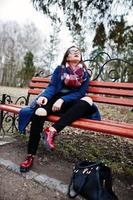 Young girl smoking cigarette outdoors sitting on bench. Concept of nicotine addiction by teenagers. photo