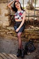 Young goth girl on black leather skirt and high heels punk shoes with backpack posed against iron fence. photo