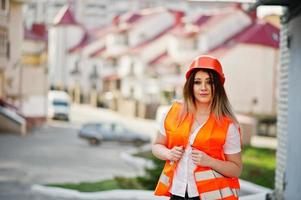 mujer ingeniera constructora con chaleco uniforme y casco protector naranja contra el nuevo edificio. tema de bloque de vivienda de propiedad.
