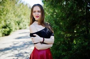 Portrait of girl with bright make up with red lips, black choker necklace on her neck and red leather skirt. photo