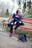 Young girl smoking cigarette outdoors sitting on bench. Concept of nicotine addiction by teenagers. photo