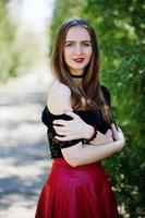 retrato de niña con maquillaje brillante con labios rojos, collar de gargantilla negra en el cuello y falda de cuero rojo. foto