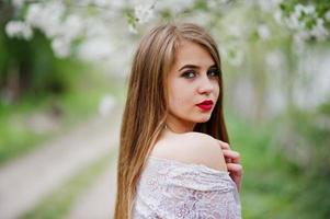 Portrait of beautiful girl with red lips at spring blossom garden, wear on red dress and white blouse. photo