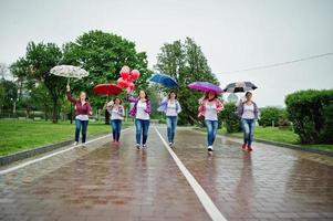 grupo de seis chicas corren y se divierten en la despedida de soltera, con paraguas bajo la lluvia y globos. foto