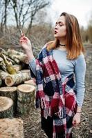 Young girl smoking cigarette outdoors background wooden stumps. Concept of nicotine addiction by teenagers. photo