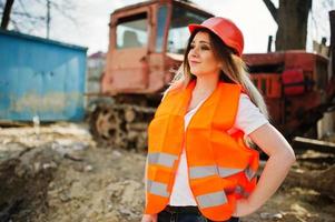 mujer ingeniera constructora con chaleco uniforme y casco protector naranja contra bulldozer. foto