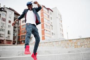 Portrait of jumping stylish african american man on sportswear, cap and glasses. Black men emotion model street fashion. photo