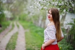 Portrait of beautiful girl with red lips at spring blossom garden, wear on red dress and white blouse. photo