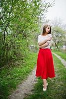 Portrait of beautiful girl with red lips at spring blossom garden, wear on red dress and white blouse. photo