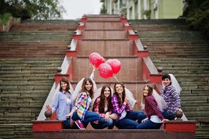 Group of six girls having fun at hen party, with balloons under rain at stairs of city. photo