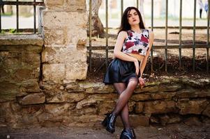 Young goth girl on black leather skirt and high heels punk shoes posed against iron fence. photo