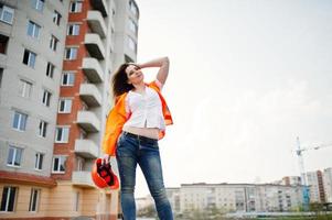 mujer ingeniera constructora con chaleco uniforme y casco protector naranja contra nuevos edificios.