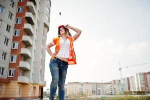 mujer ingeniera constructora con chaleco uniforme y casco protector naranja contra nuevos edificios. foto