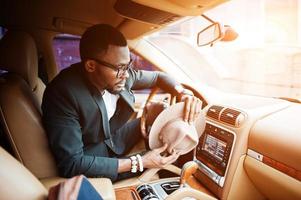 Stylish black man sitting behind the wheel of luxury car. Rich african american businessman. photo