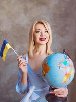 beautiful attractive cheerful blonde Slavic woman holding globe and ukrainian flag. photo