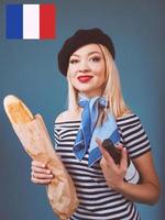 Retrato de una hermosa mujer francesa rubia en boina, bufanda, espalda y camisa blanca, con una botella de vino y pan baguette en sus brazos con la bandera francesa en el fondo foto
