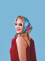 stylish smiling cheerful fancy blonde woman with make up in neckerchief and sunglasses on blue background photo