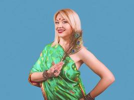 bella y atractiva mujer rubia europea sonriente vestida con un vestido nacional indio con plumas de pavo real, pulseras, accesorios. foto