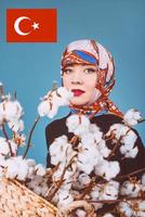 oriente a la mujer en un colorido pañuelo sosteniendo una cesta con ramas de algodón sobre fondo azul. recolector de algodón foto