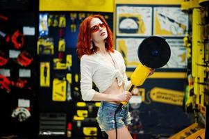Red haired model posed with large angle grinder at store or household shop of working tools. photo