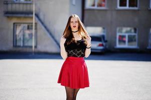 Portrait of girl with black choker necklace on her neck and red leather skirt at street of city. photo