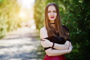 Portrait of girl with bright make up with red lips, black choker necklace on her neck and red leather skirt. photo