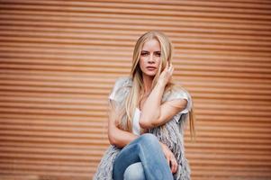 Stylish blonde woman wear at jeans and girl sleeveless with white shirt against shutter background. Fashion urban model portrait. photo