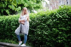 Stylish blonde woman wear at jeans and girl sleeveless with white shirt against bushes at street. Fashion urban model portrait. photo