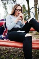 Young girl smoking cigarette outdoors sitting on bench. Concept of nicotine addiction by teenagers. photo