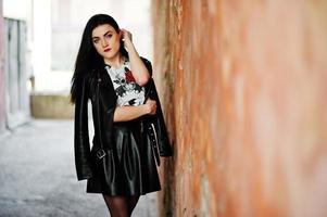 Young goth girl on black leather skirt and jacket against grunge wall. photo