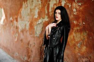 Young goth girl on black leather skirt and jacket against grunge wall. photo