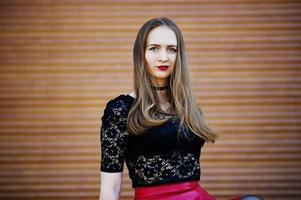 Portrait of girl with black choker necklace on her neck and red leather skirt against orange shutter. photo