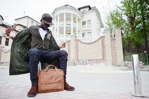 Portrait of stylish african american man wear on sunglasses and cap with handbag outdoor. Street fashion black man. photo