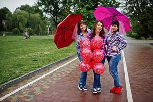 grupo de tres chicas divirtiéndose en la despedida de soltera, con paraguas bajo la lluvia y globos. foto