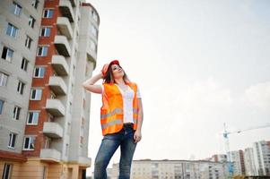 mujer ingeniera constructora con chaleco uniforme y casco protector naranja contra nuevos edificios.