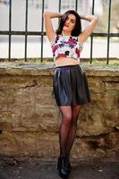 Young goth girl on black leather skirt and high heels punk shoes against iron fence. photo